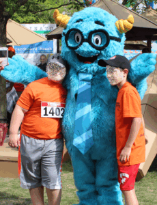 Image of a blue monster mascot at an event posing for a photo with two young children